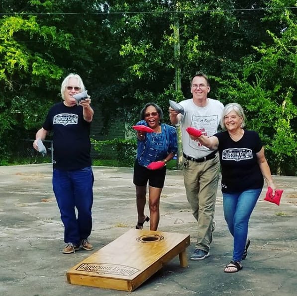 Four people holding beanbags beside a cornhole board outdoors