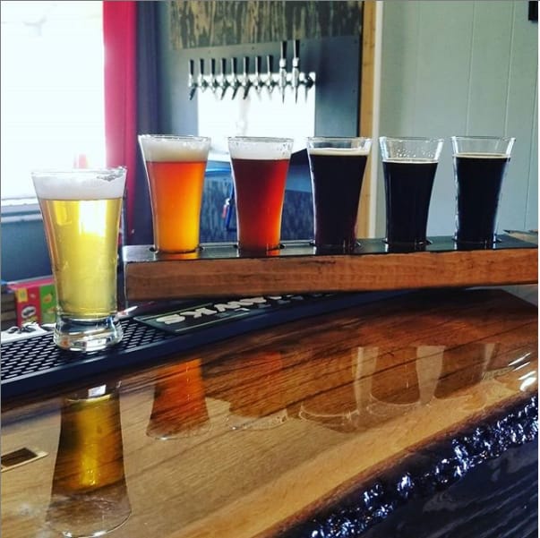 A flight of beers ranging from pale gold to dark brown on the wooden taproom bar